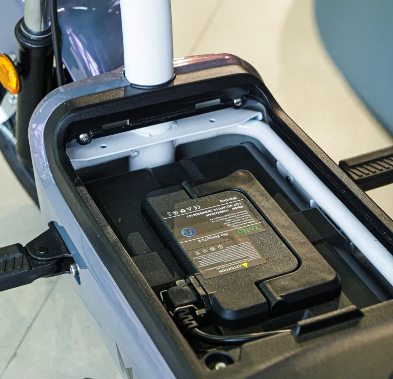 A bateria de lítio 60V20Ah fica abrigada em um compartimento sob o assento, protegida contra impactos e bem posicionada para otimizar o espaço da scooter. Fácil acesso para conectar o carregador e garantir que a Joyzinha esteja sempre pronta para rodar.